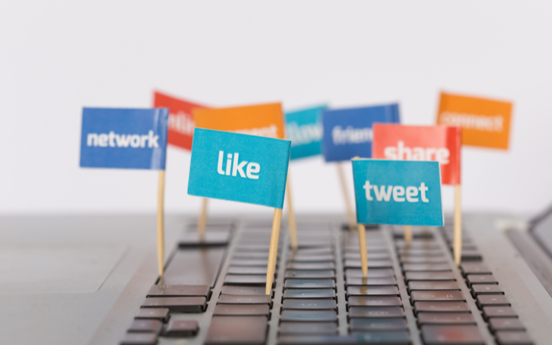 Colourful flags with text like "like," "tweet," and "share" placed on a keyboard, symbolising social media opportunities for Donau Soja members.